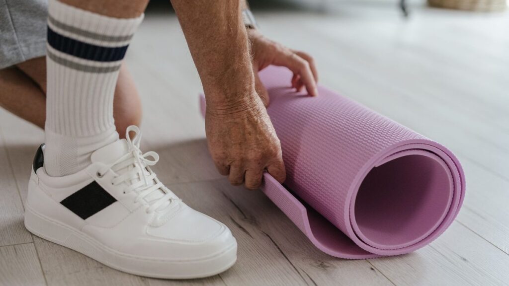 Main déroulant un tapis d'entraînement sur un parquet clair